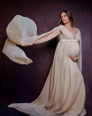 Flowing cream-colored maternity gown with billowing fabric against dark backdrop.
