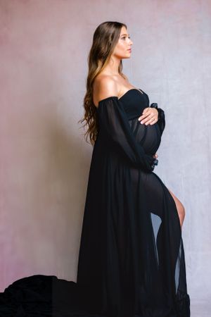 Elegant maternity portrait in black off-shoulder dress with side slit.