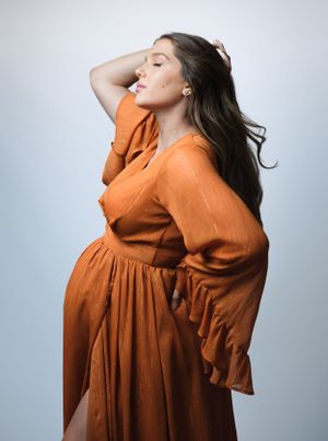 Side profile of woman in rust-colored dress with flowing sleeves.