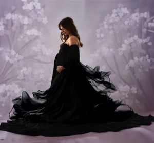 Dramatic maternity silhouette in flowing black gown against purple floral backdrop.