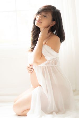 Artistic maternity portrait featuring a woman in delicate white lace dress.
