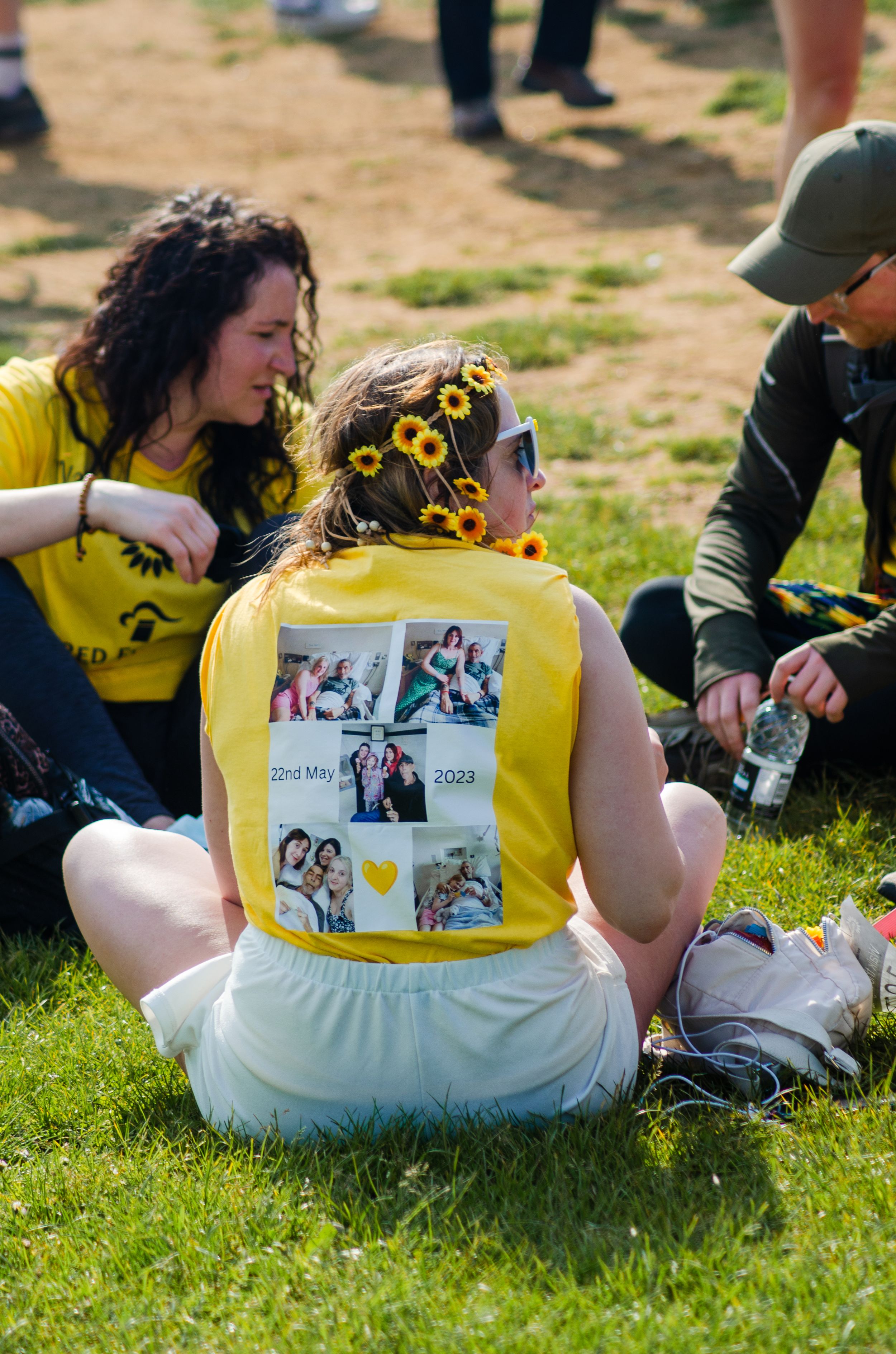 Group relaxing on grass wearing yellow shirts with sunflower decorations at outdoor event.