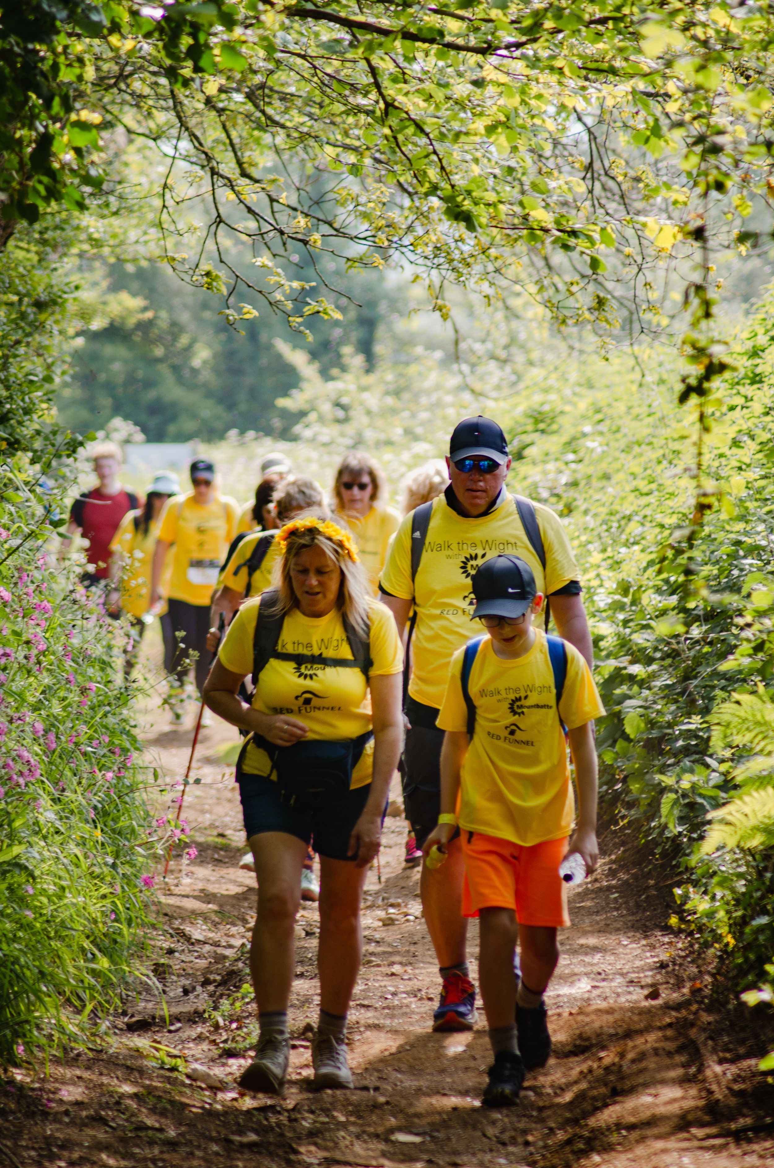 Group of walkers in yellow shirts hiking through tree-lined nature trail.