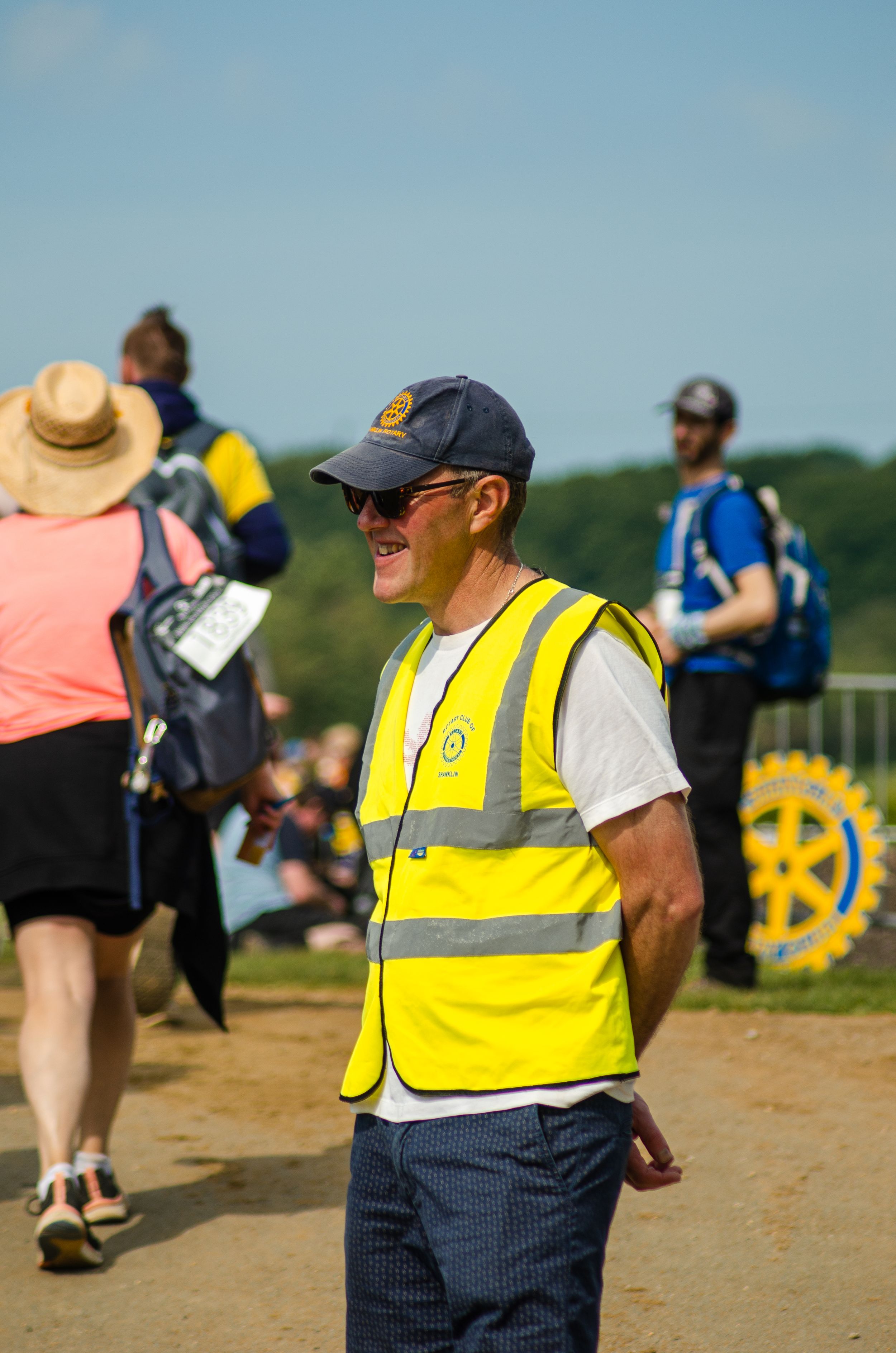 Event volunteer in high visibility yellow vest supervises outdoor community gathering.