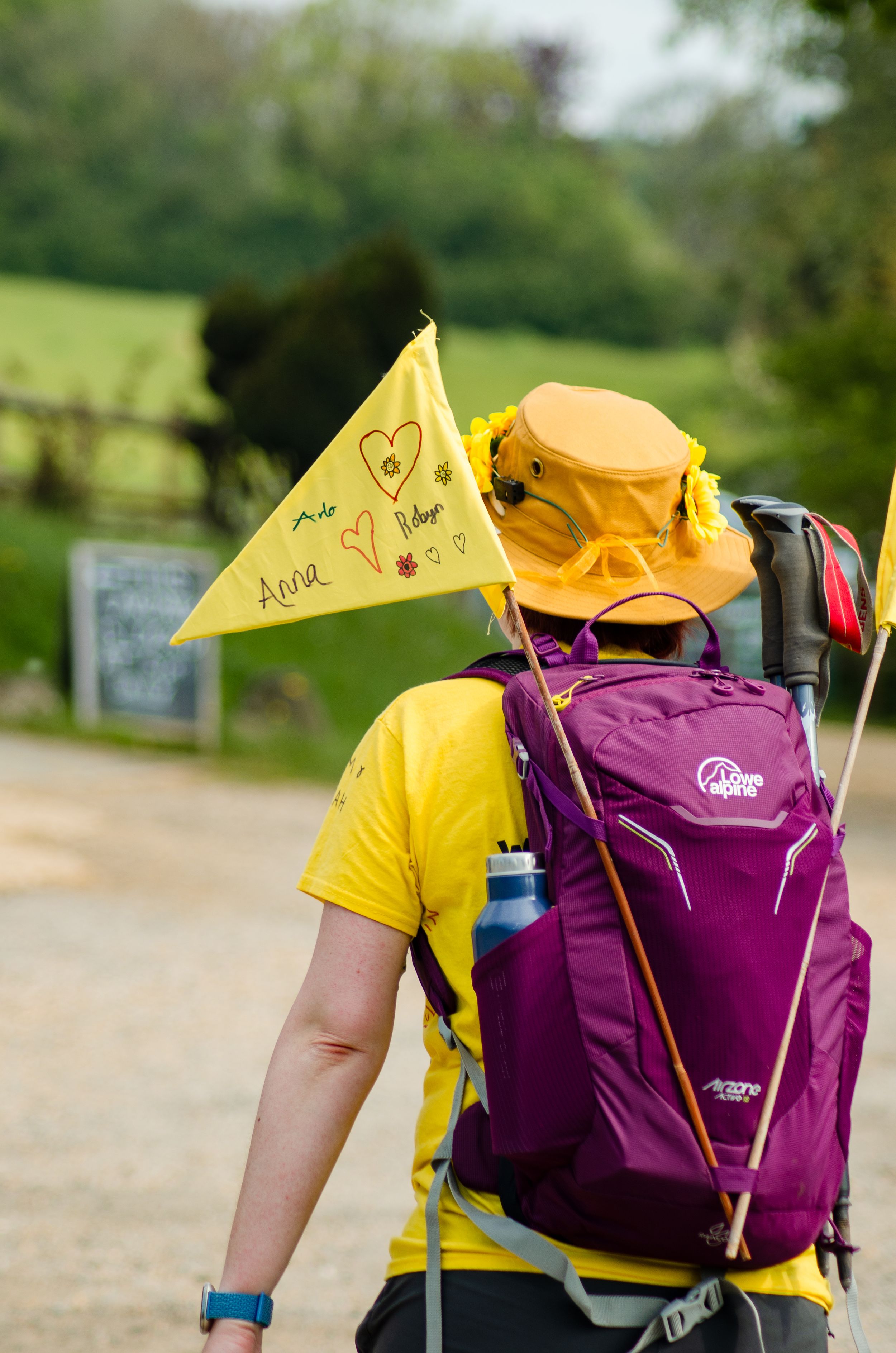Hiker wearing purple backpack with decorative yellow flag on nature trail.