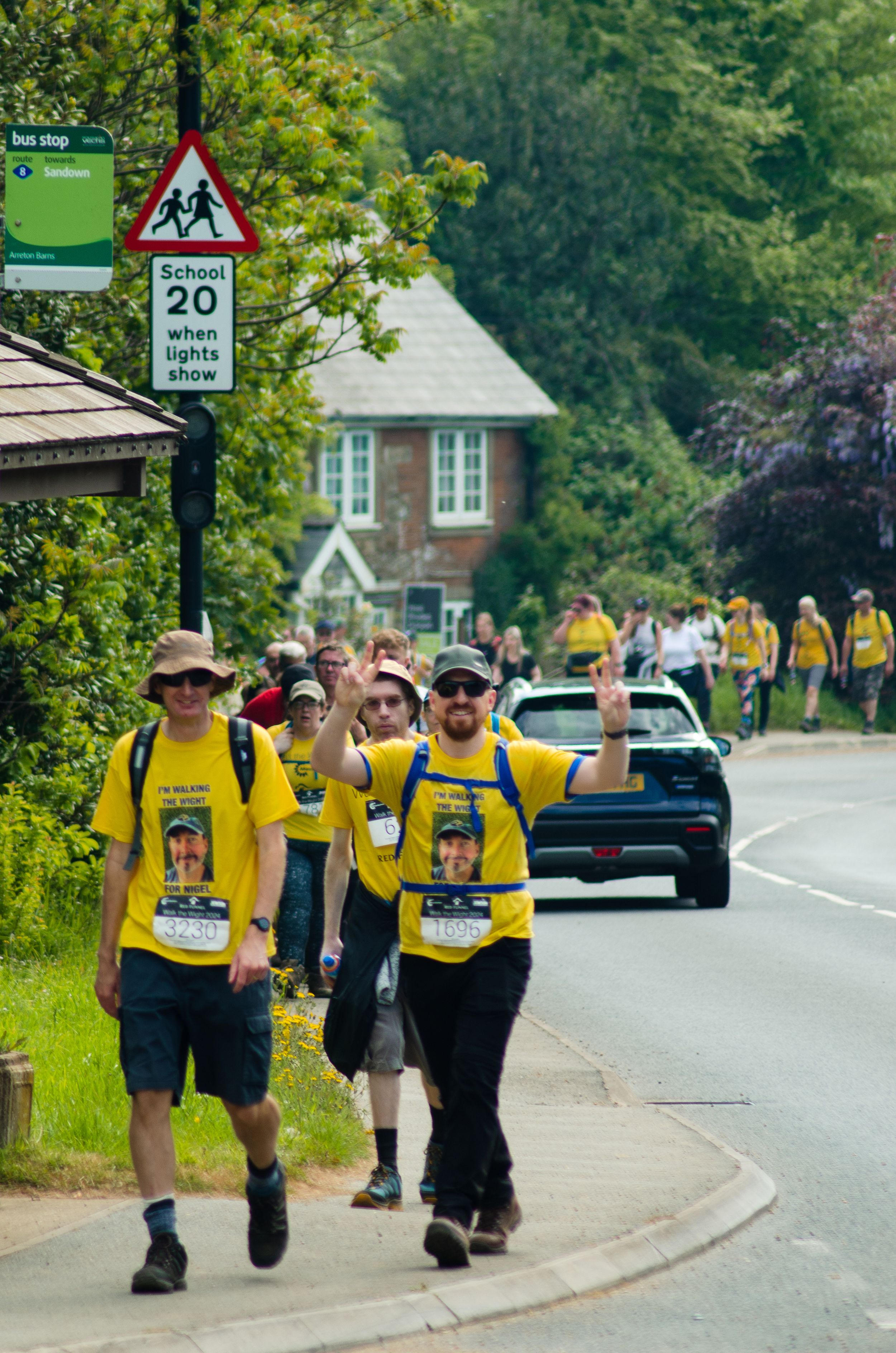 Group of participants in yellow shirts walking along a suburban road with 20mph speed limit sign.