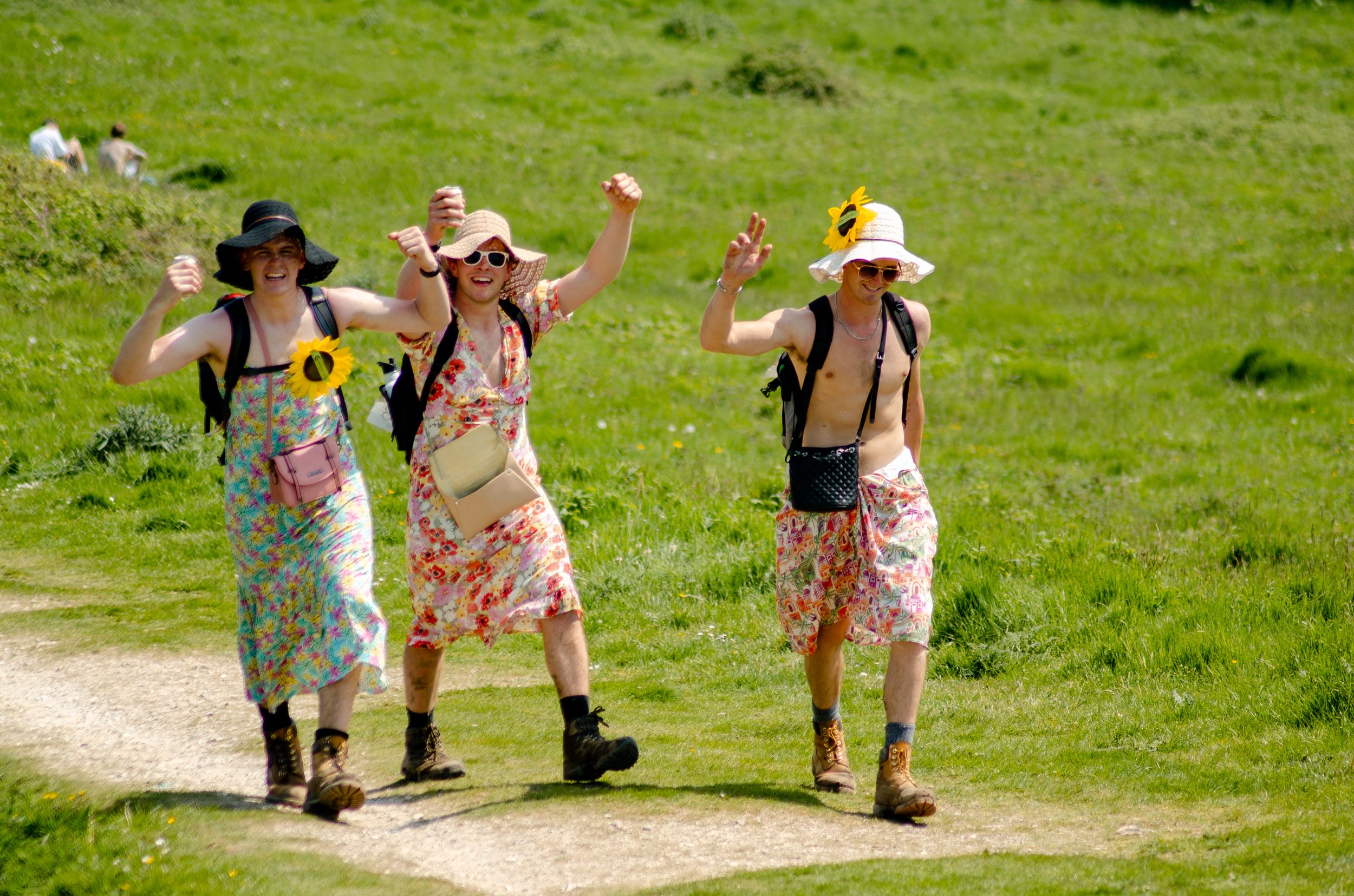 Three people in floral dresses and sunhats celebrating on hiking trail.