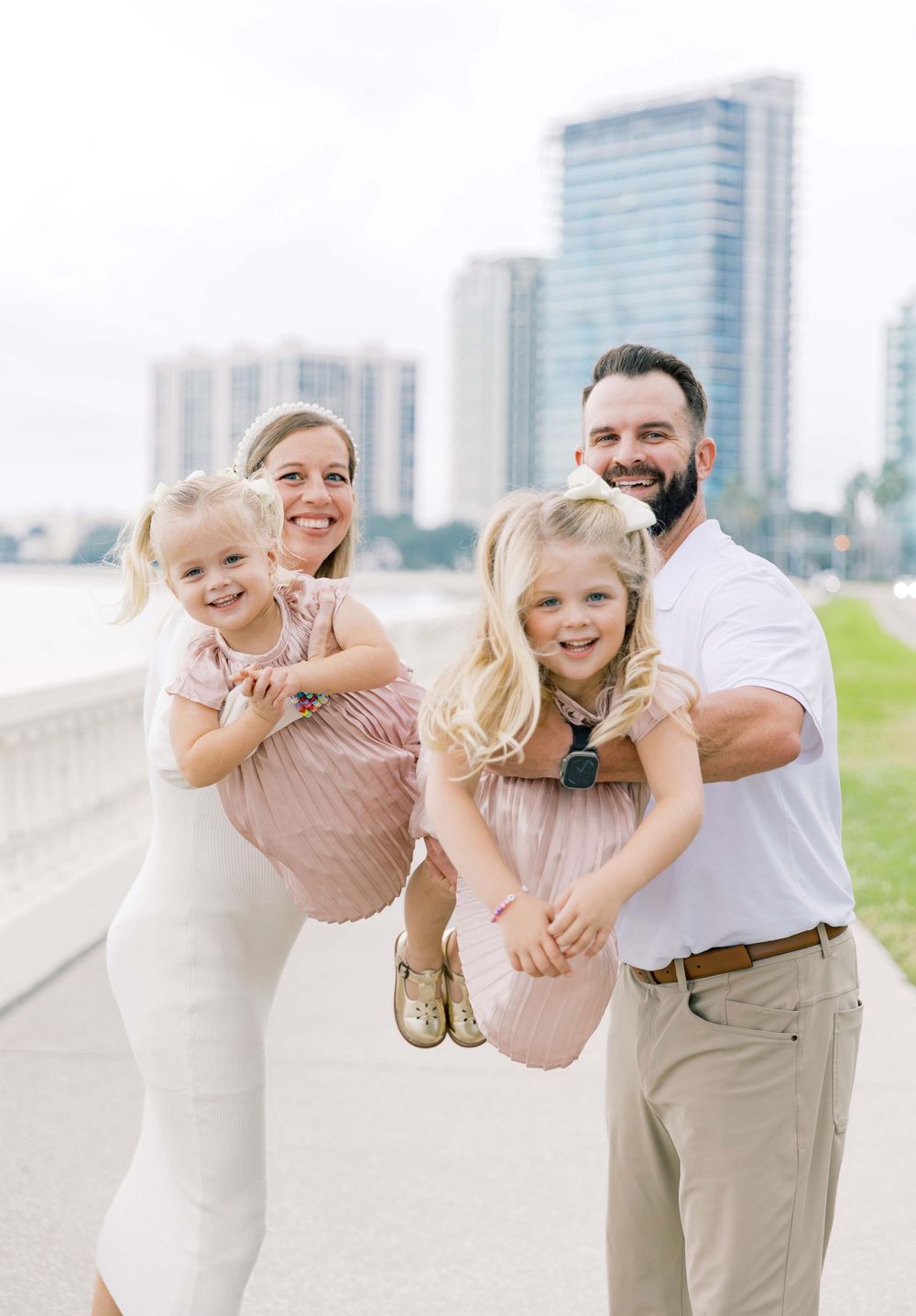 Happy family playing and posing together on a waterfront walkway with city skyline behind them.