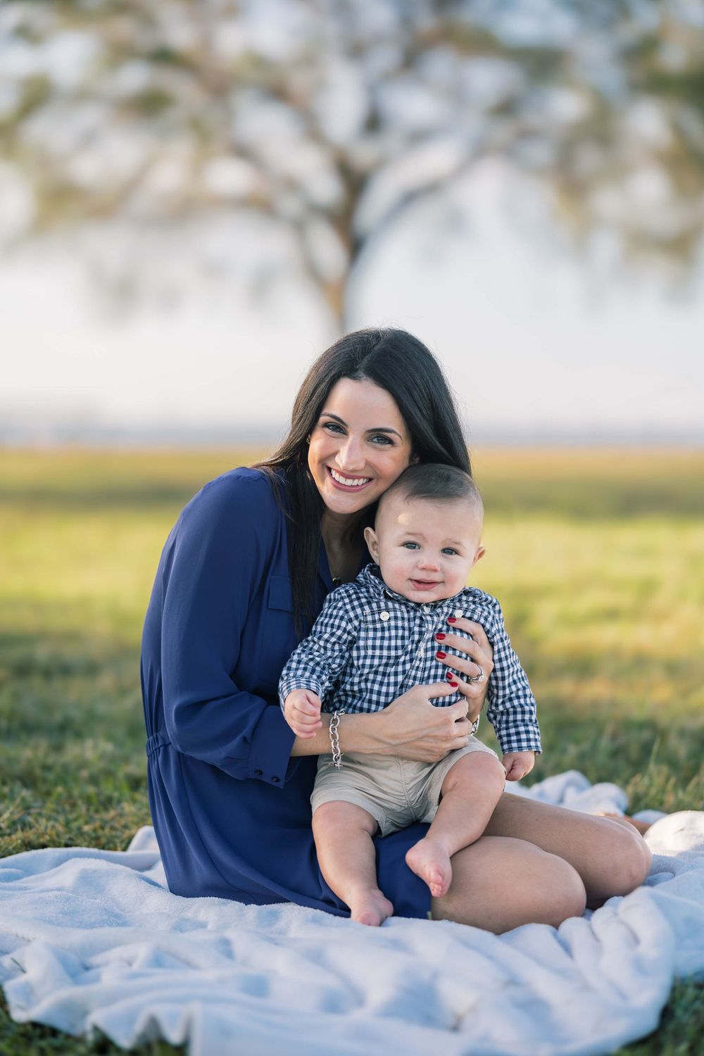 A peaceful outdoor portrait of a mother and baby sitting on a blanket in golden sunlight.