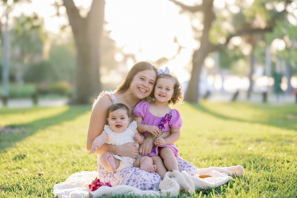 A joyful outdoor family portrait on a blanket in a sun-dappled park during golden hour.