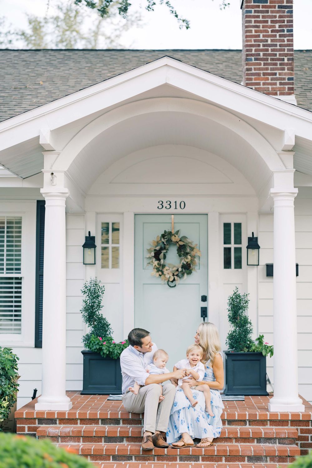 Family sits together on front porch steps of house number 3310.