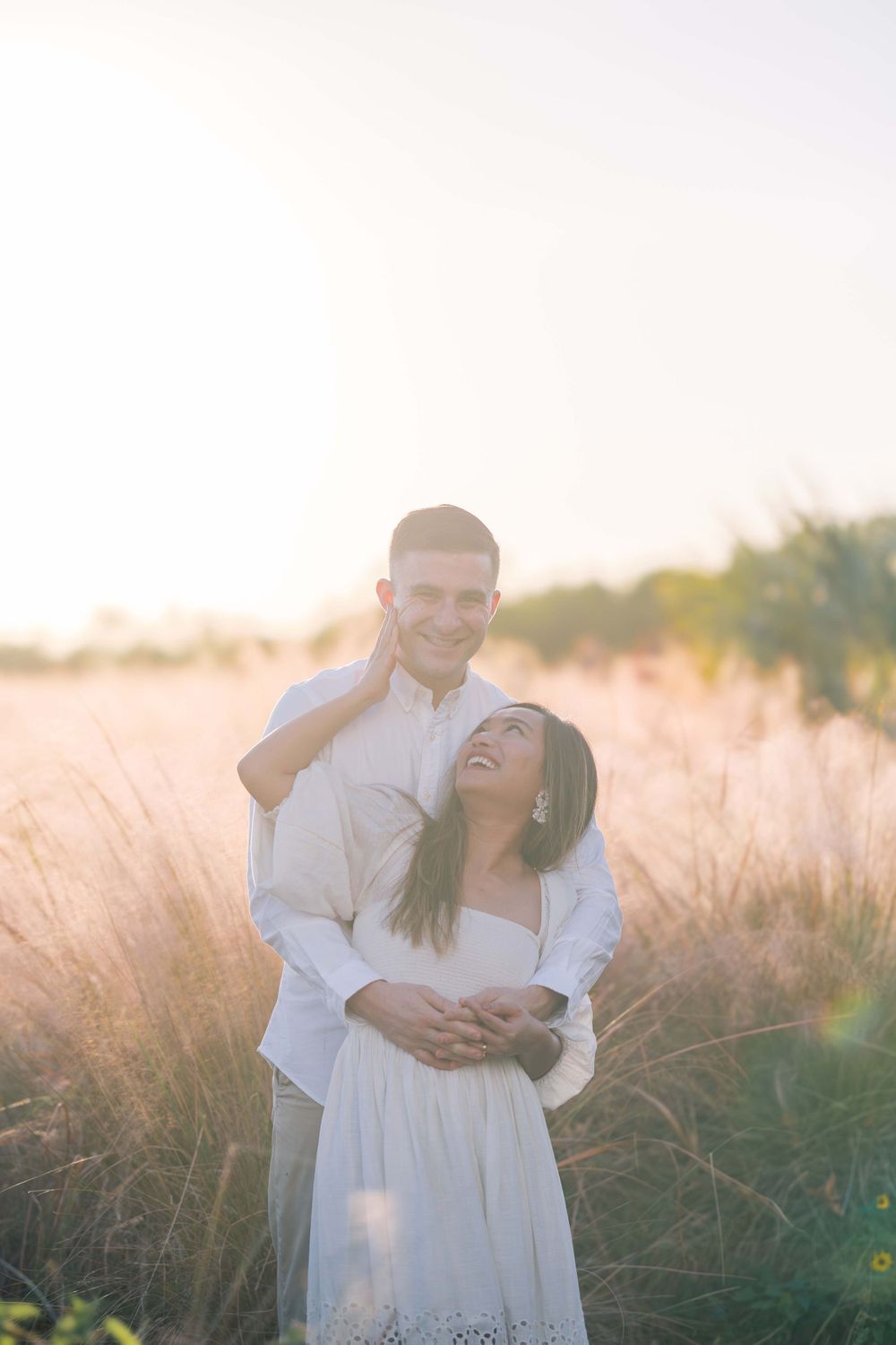 Couple shares intimate moment while embracing in golden field at sunset.