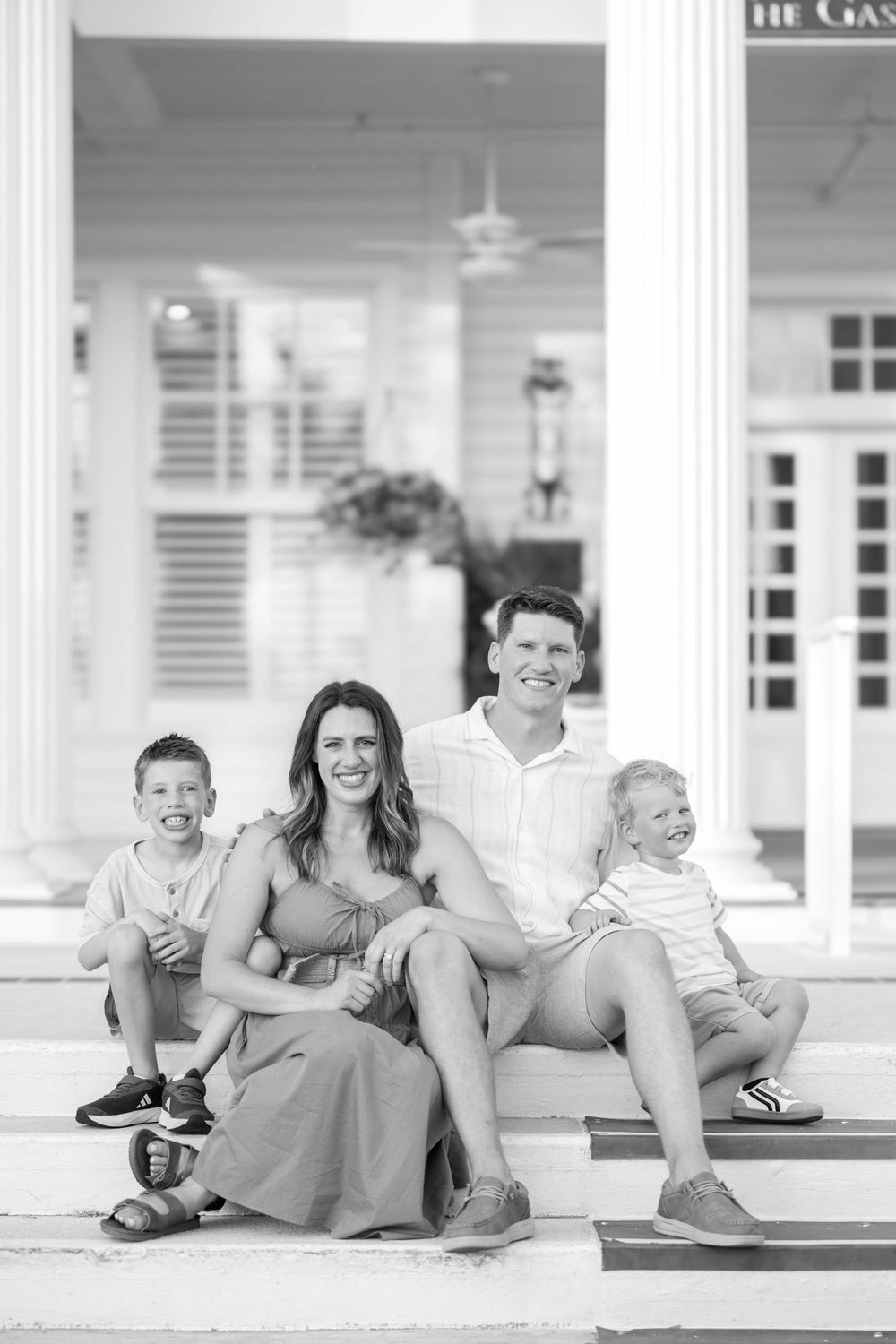 A family sits together on outdoor porch steps in a black and white portrait photo.