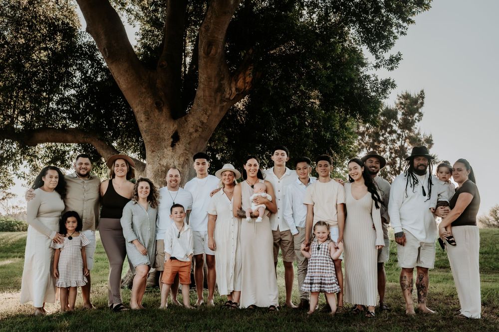 Large family group portrait standing together under a big tree during golden hour outdoors.