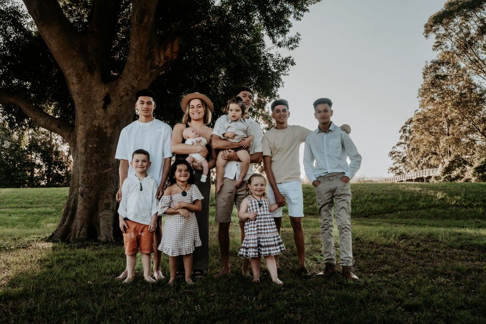 Large extended family group portrait outdoors under a big tree on a sunny green lawn.