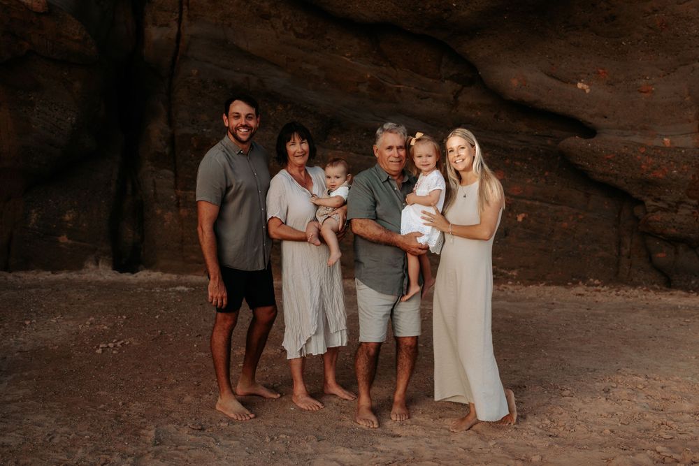 Family of six posing barefoot in front of red rock cave walls holding two young children.