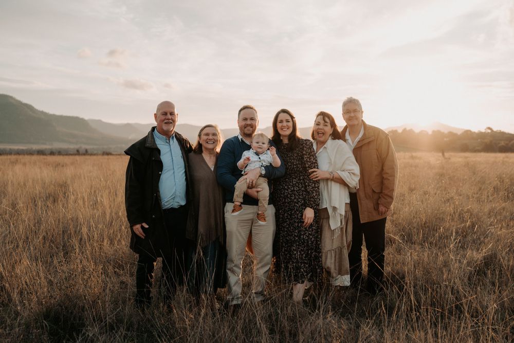 Multi-generational family of seven posing in a golden field at sunset with mountains in the background.