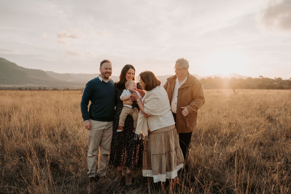Family of five sharing a warm moment in a sunlit golden field at sunset, with parents and grandparents.