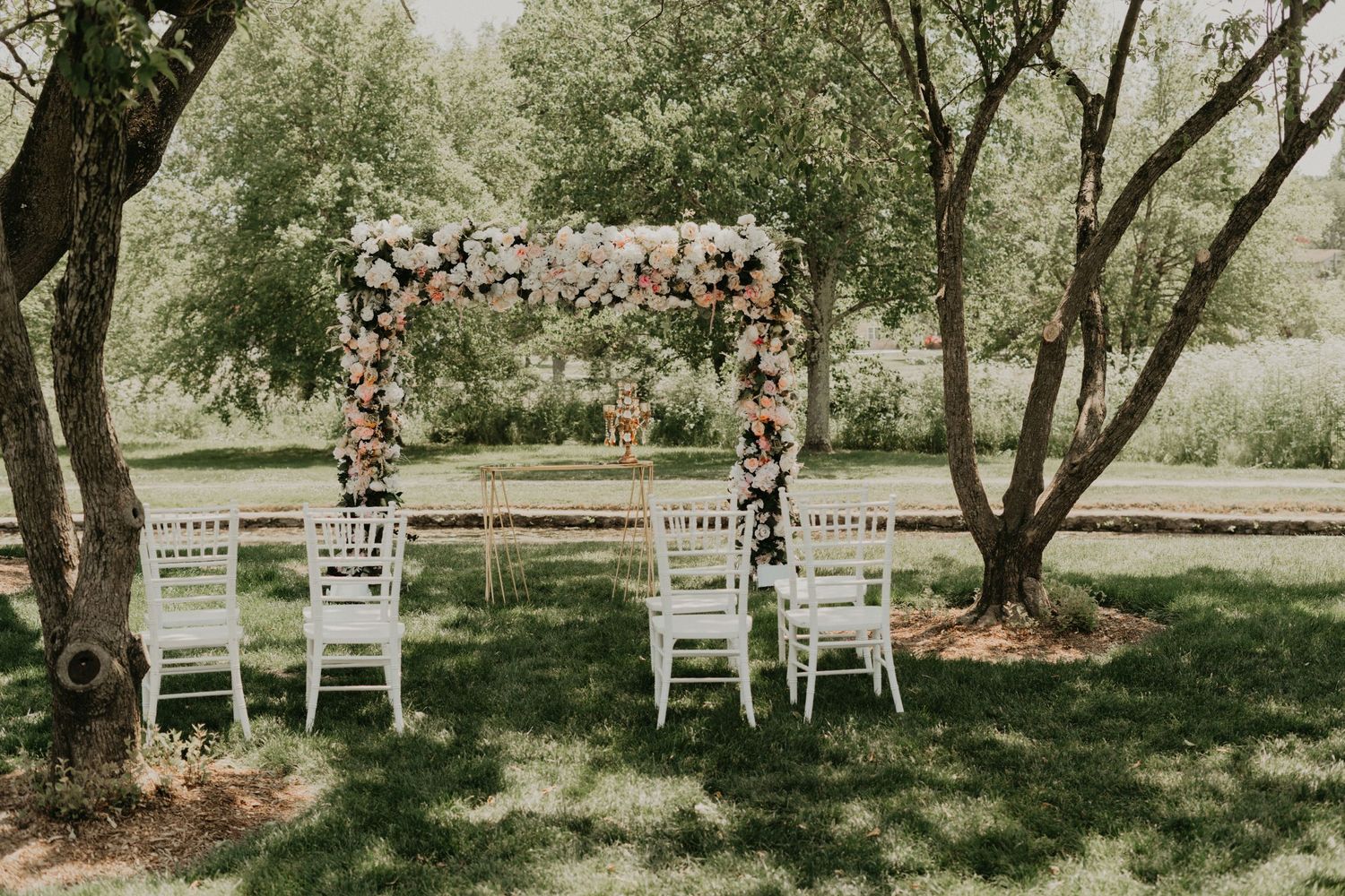Floral arch with white chairs set up for outdoor garden wedding ceremony.
