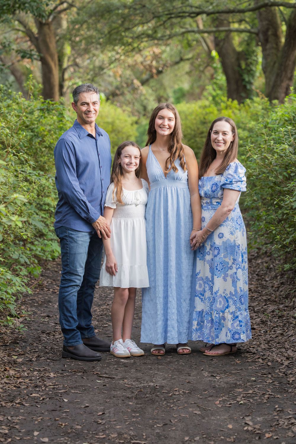 A group poses together on a wooded path wearing coordinated blue and white outfits on a summer day.