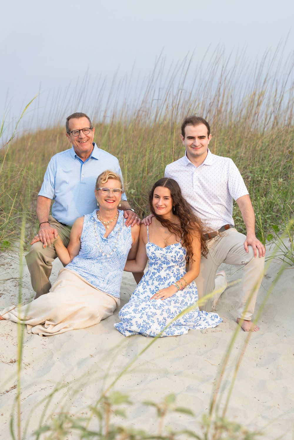 A family relaxes together on a sandy beach with sea grass in the background during a sunny day.