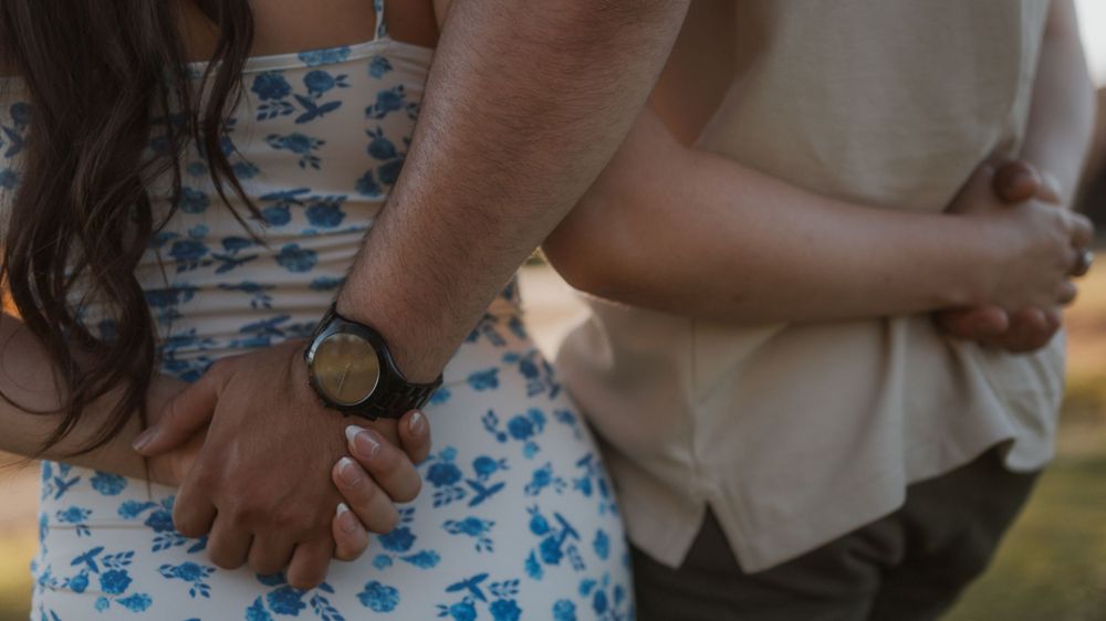 Two people standing closely side by side, with arms wrapped around each other.