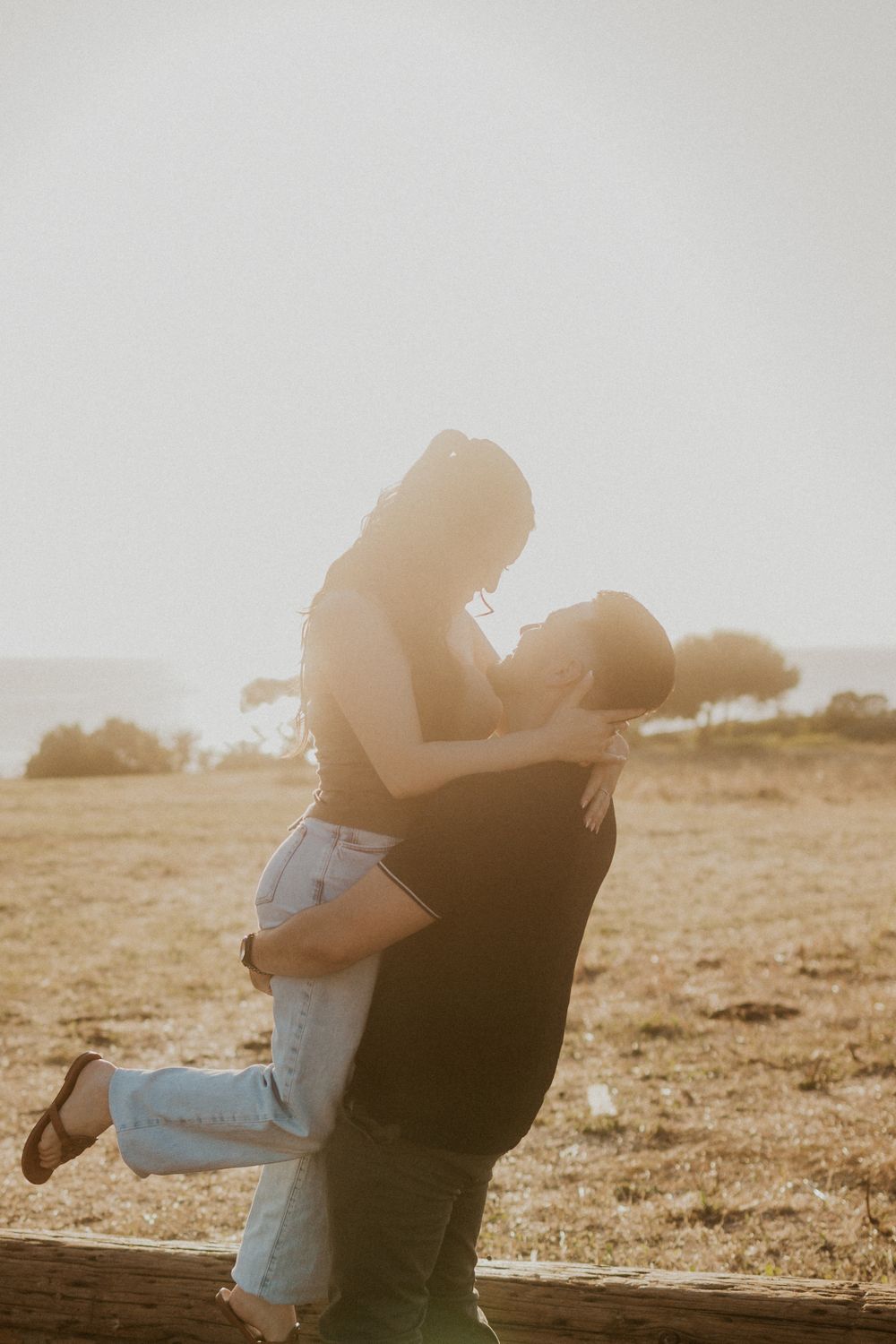 Man lifting woman outdoors during sunset.