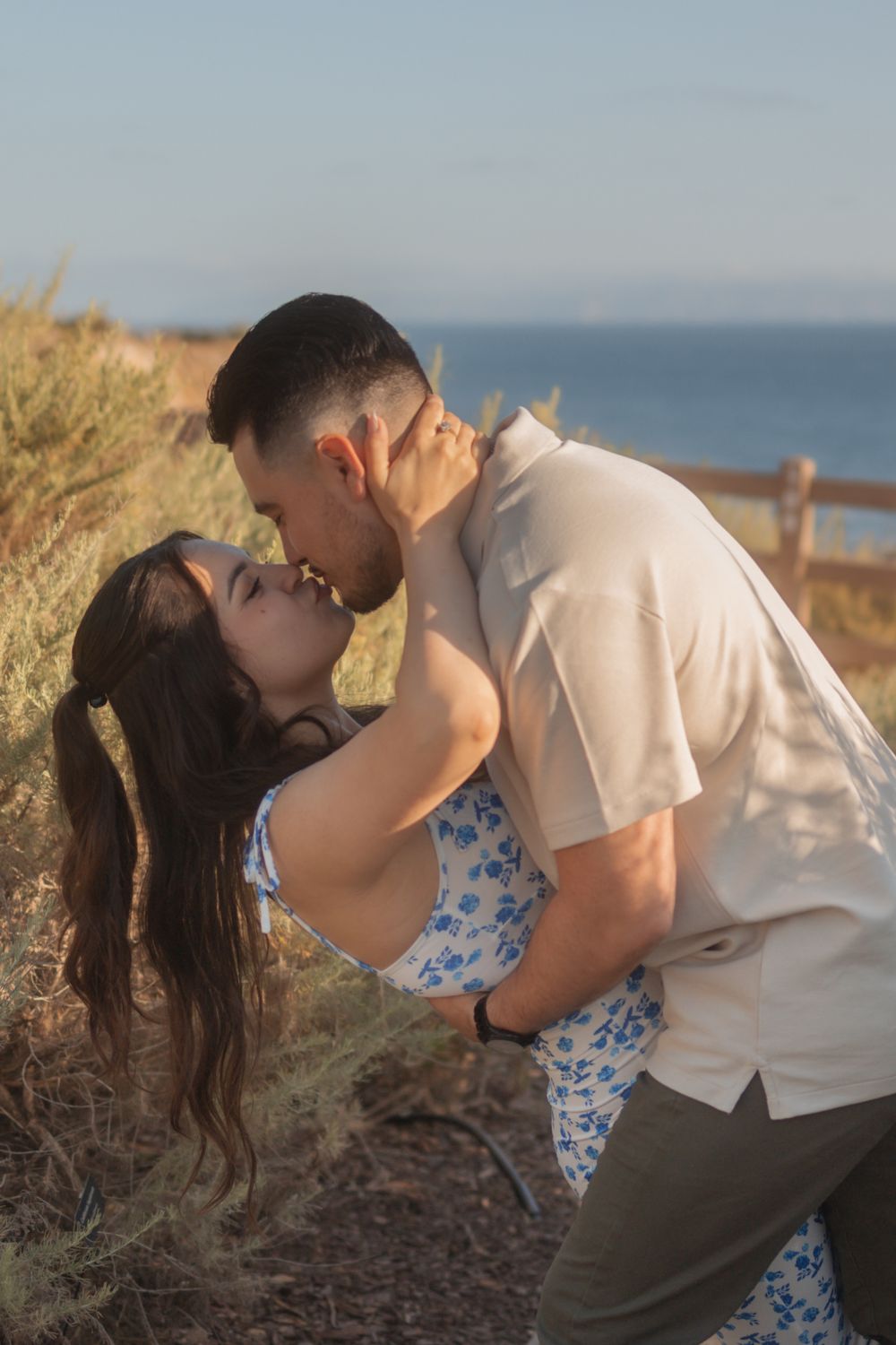 A couple kisses outdoors near the sea during golden hour.