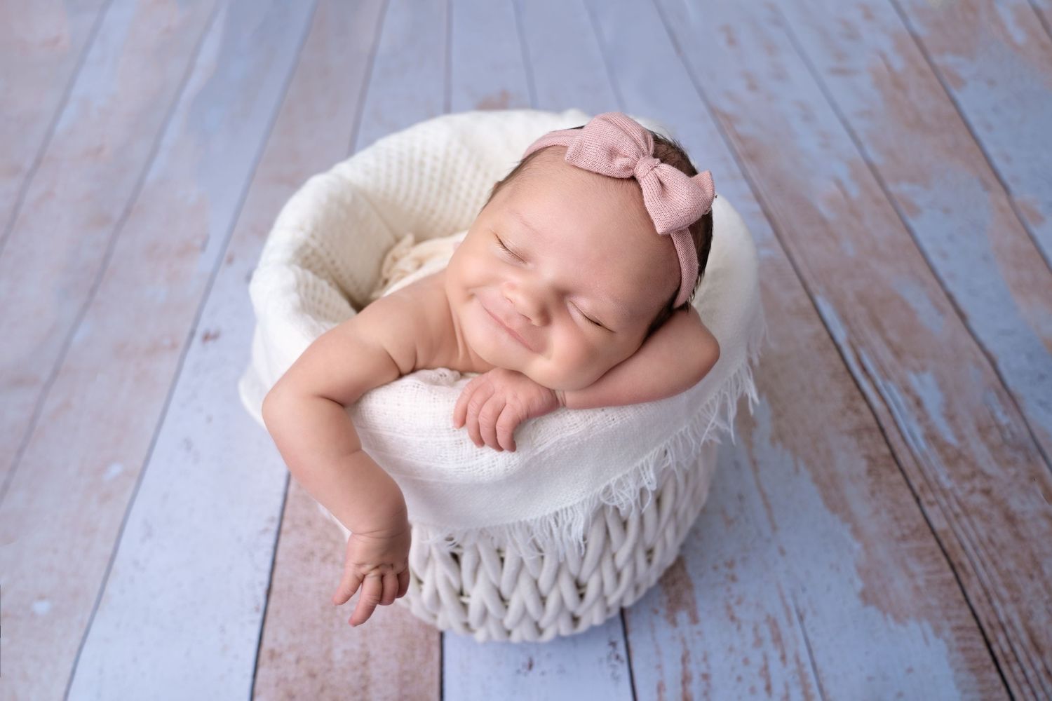 Newborn baby sleeping peacefully in white bowl on rustic wooden floor.
