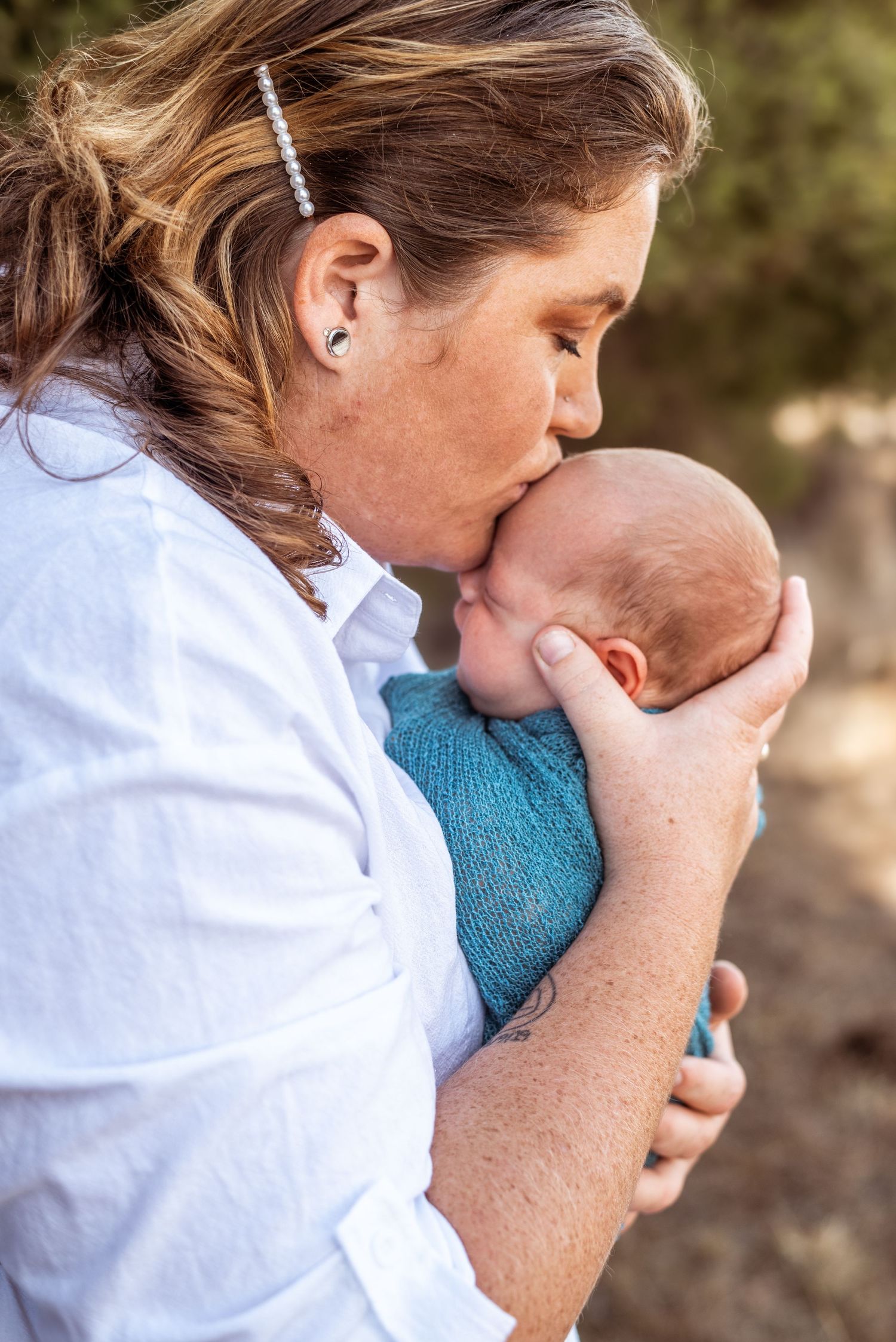 Intimate moment as parent gives gentle kiss to newborn baby wrapped in teal blanket.