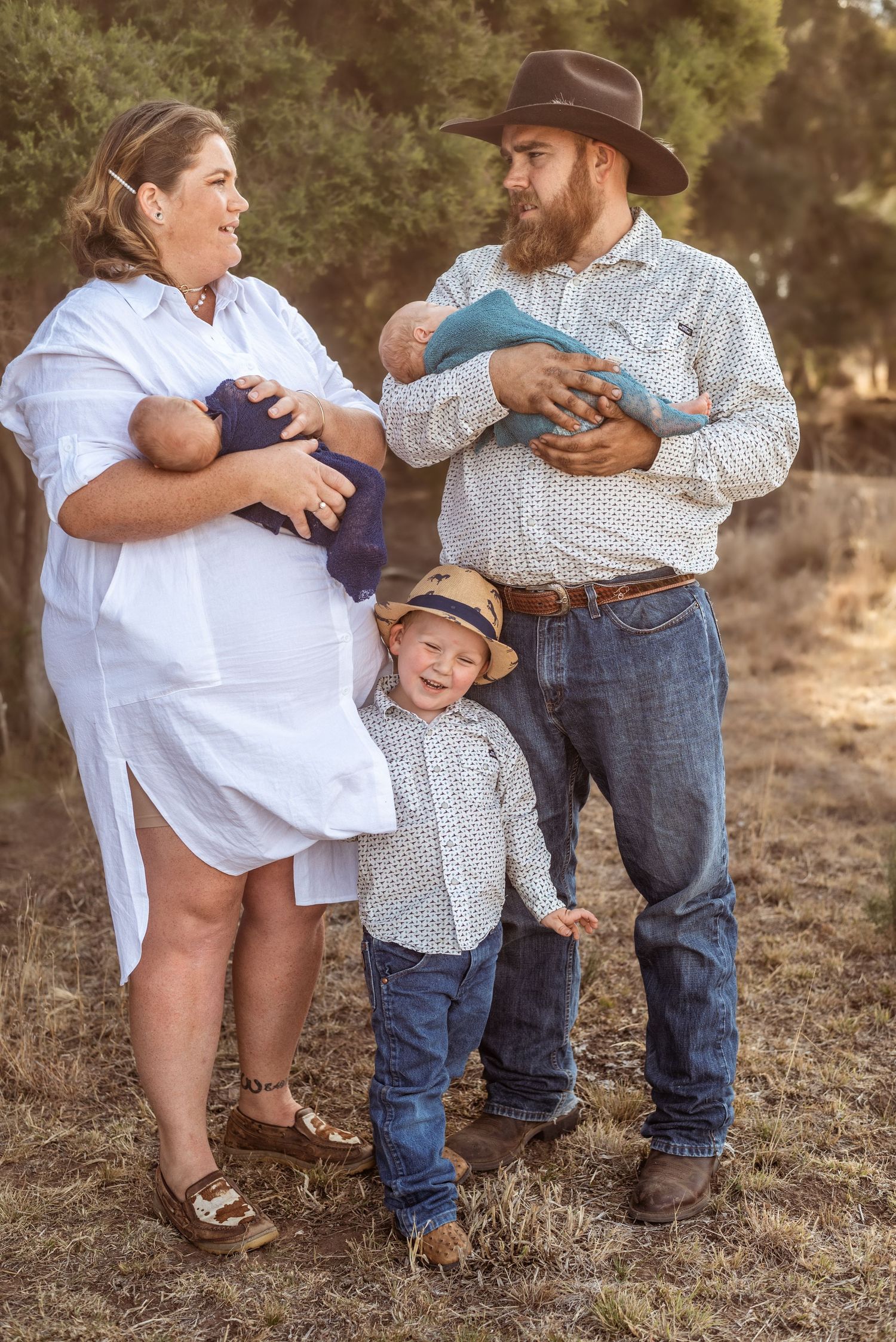 Family outdoor portrait with parents and children in coordinating outfits against natural background.