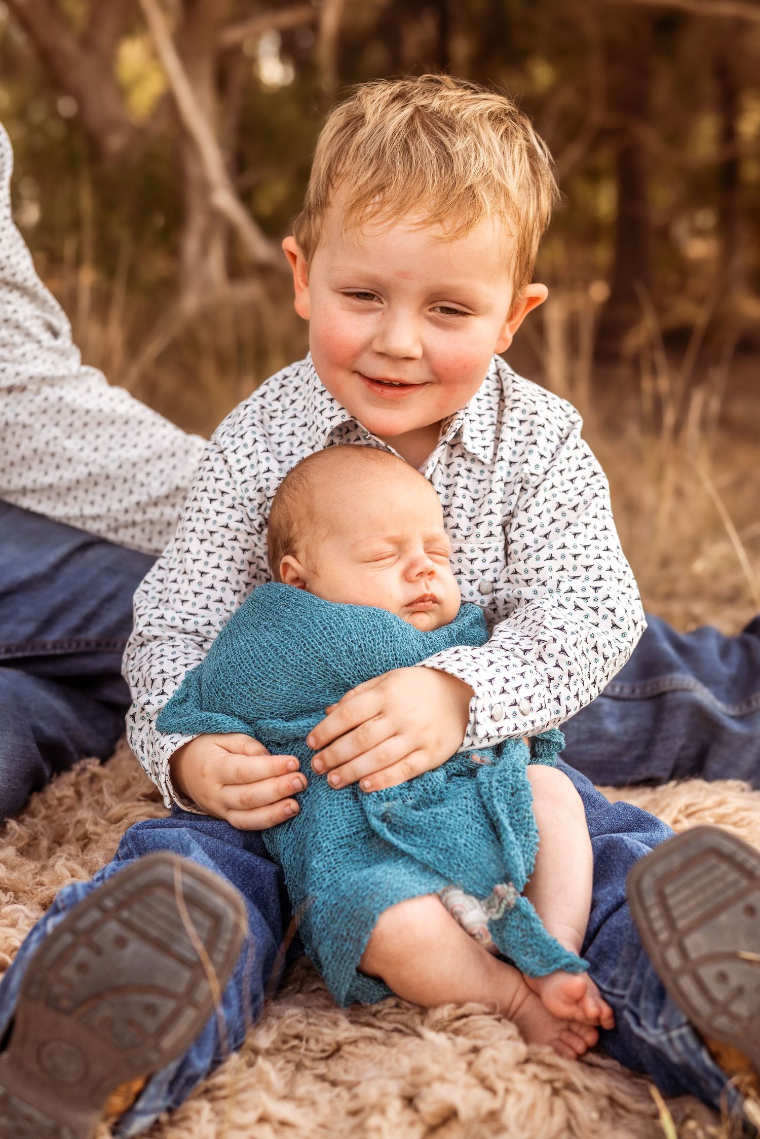 Heartwarming moment between siblings as older child holds sleeping newborn wrapped in teal blanket.