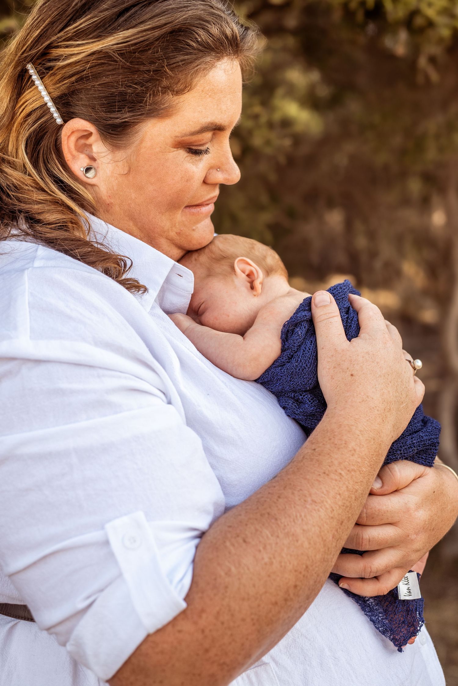 Peaceful moment as parent in white shirt holds sleeping newborn wrapped in navy blanket.