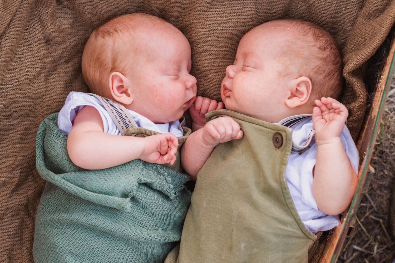 Two babies in green and white outfits lying side by side sleeping peacefully.