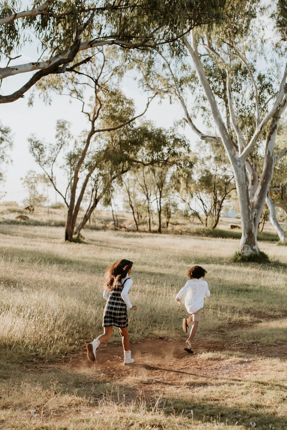 girl and boy run through the trees as the sunsets in Mount Isa