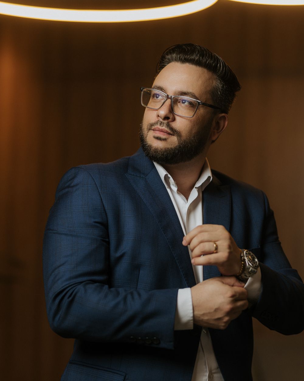 Business portrait of person in navy suit adjusting cufflinks in warm-toned professional setting.