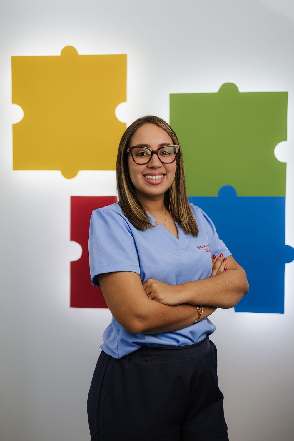 Healthcare professional in blue scrubs poses confidently against colorful puzzle piece wall decor.