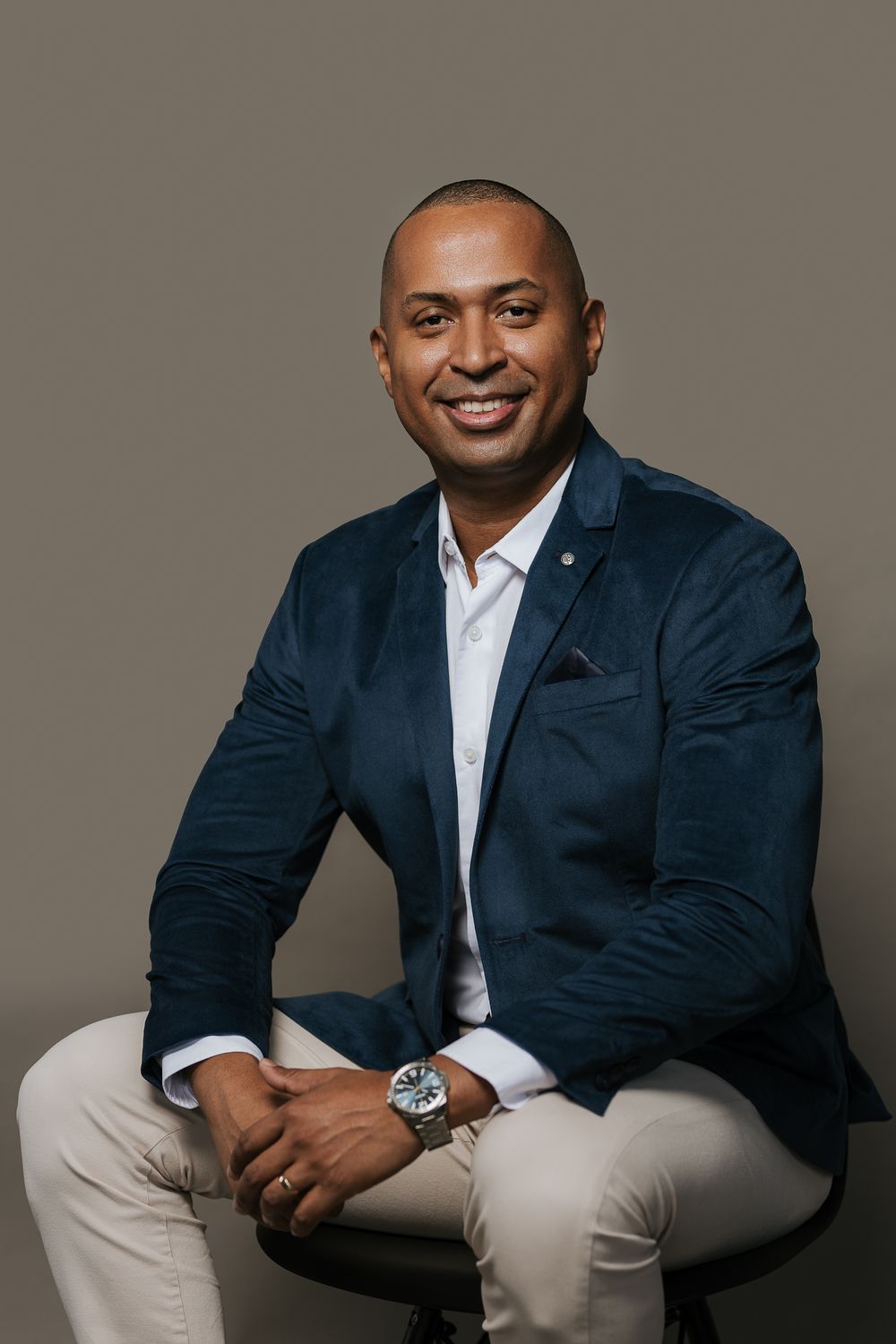 Professional business portrait in navy blazer and white shirt against neutral background.