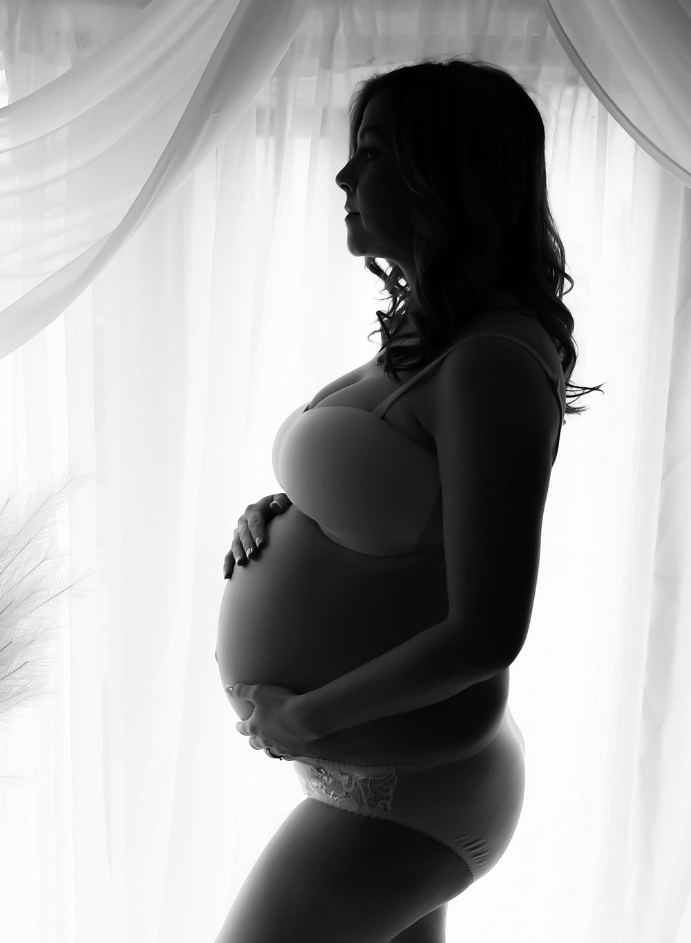 Silhouette backlit image of pregnant mother to be. Hands clasped round the bump lovingly.