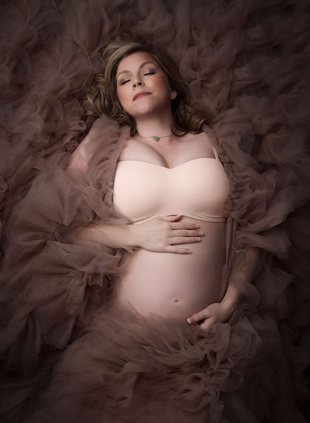 Maternity image with mum laid on the ground on her tulle dress. Eyes are closed and hands resting on the bump.