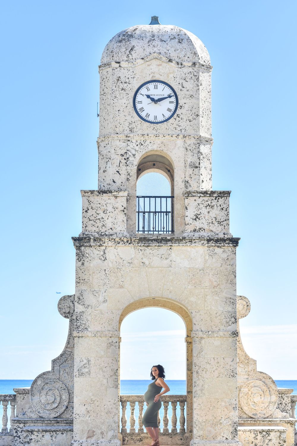 Historic clock tower with Mediterranean architectural details and ocean view in background.