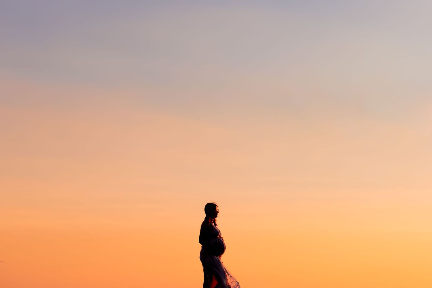 Silhouette of an expectant mother against a vibrant orange sunset sky.