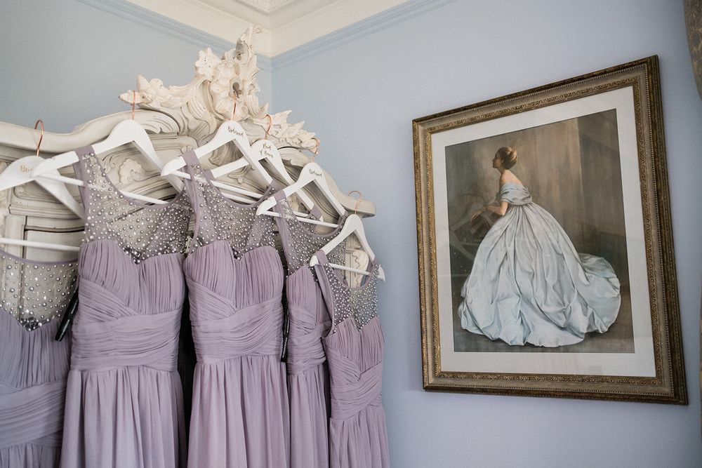 Lavender bridesmaid dresses hanging on white hangers beside framed wedding portrait.