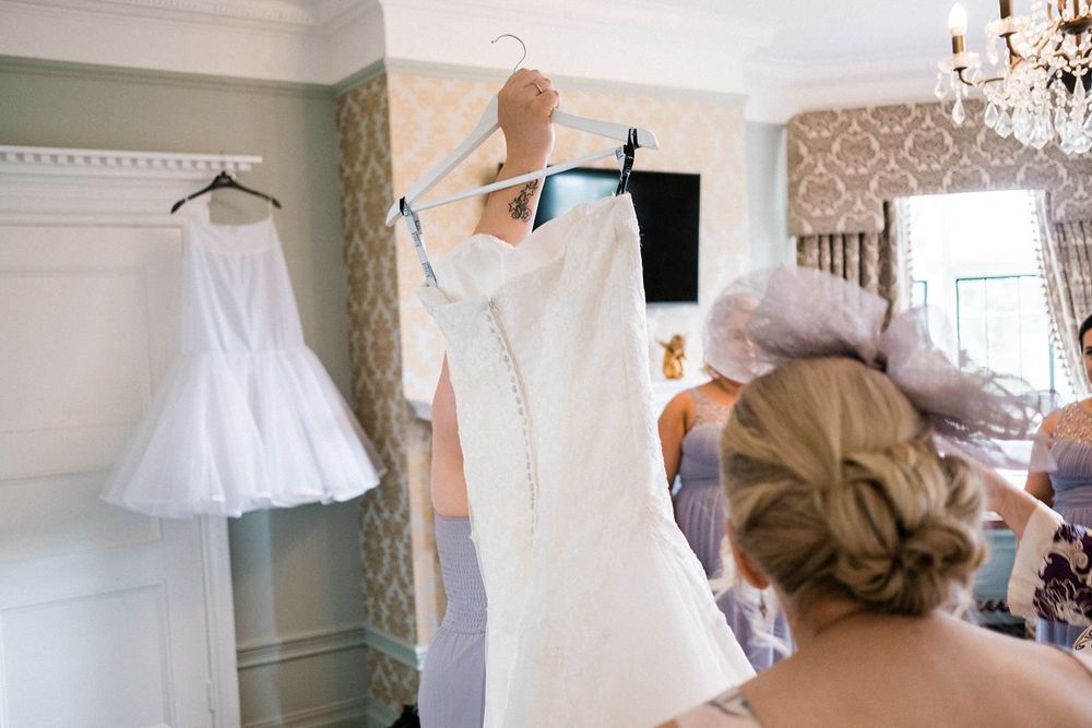 Wedding dress and petticoat hanging in an elegant room with patterned wallpaper and chandelier.