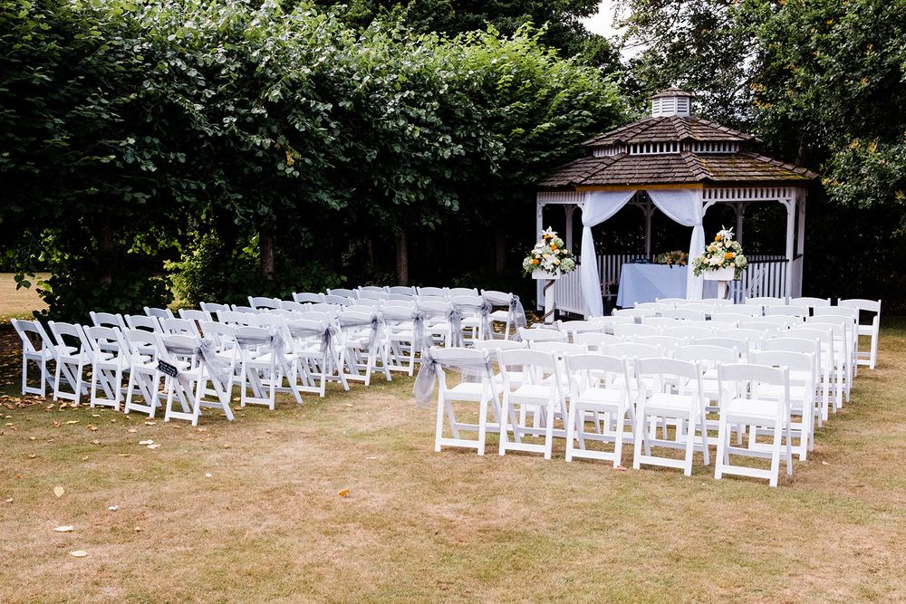 Outdoor wedding ceremony setup with white chairs arranged facing a decorated gazebo.
