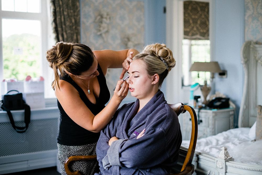 Makeup application session taking place in an elegant room with vintage wallpaper.