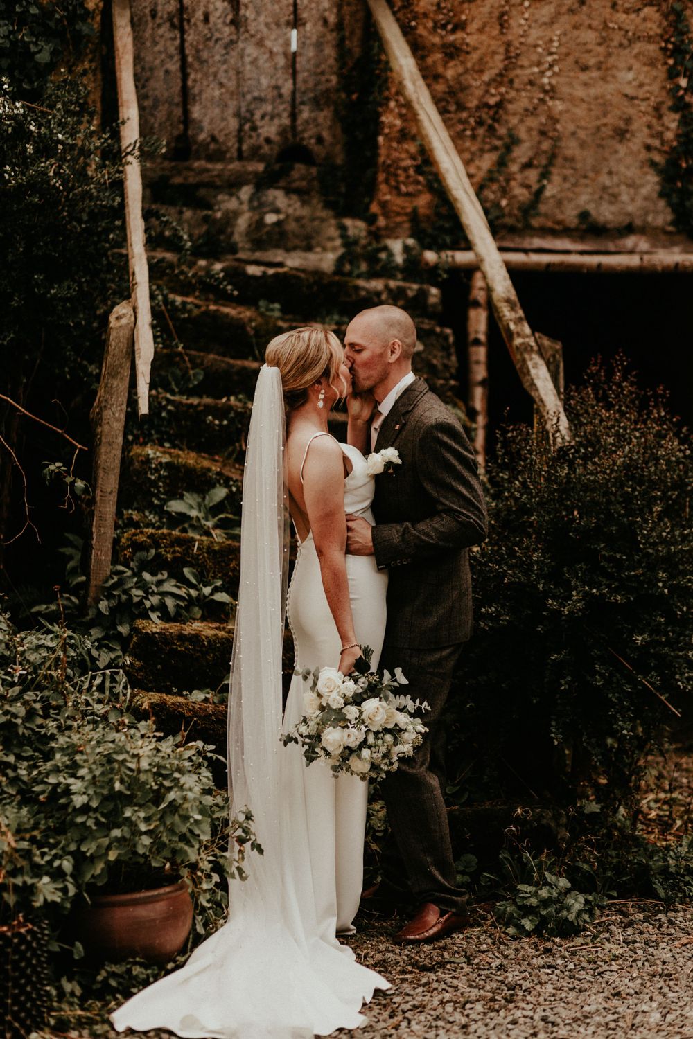 An intimate wedding portrait with white bouquet against weathered stone wall backdrop.