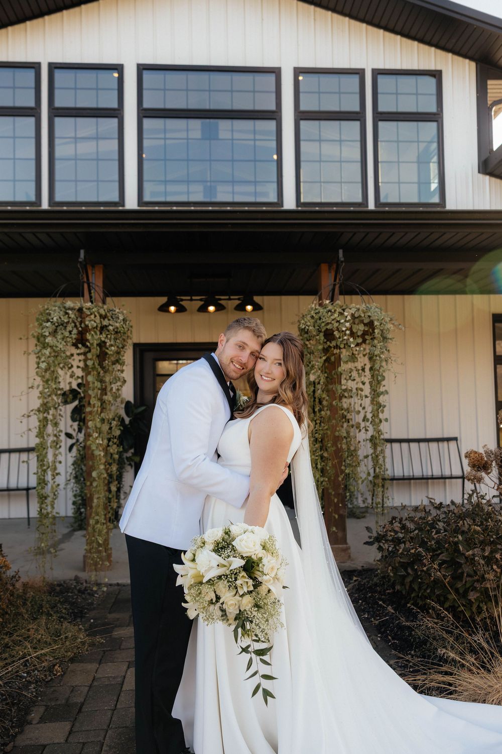 Elegant wedding couple embraces against contemporary white building with floor-to-ceiling windows.