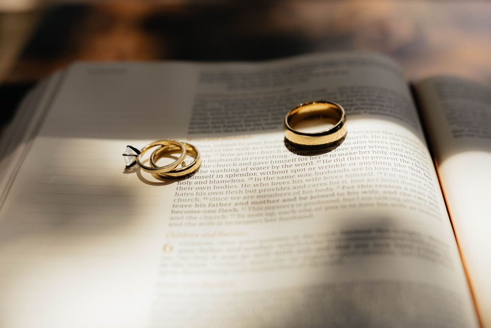 Two gold wedding bands and a diamond engagement ring resting on an open Bible page.