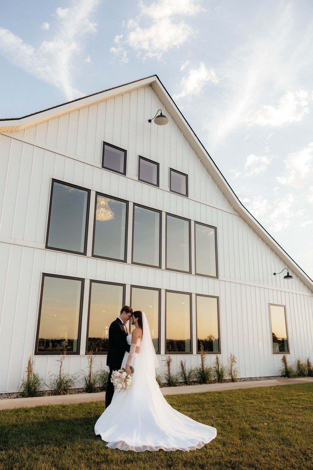 Bride and groom share a romantic moment outside a modern white barn wedding venue at golden hour.